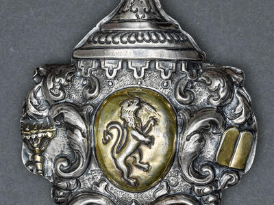 Silver amulet with designs around edge and lion in center.