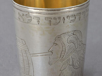 Silver cup engraved with a person in profile wearing a jester hat drinking out of a barrel. 