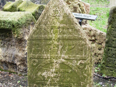 Tombstone in graveyard with triangular top, Hebrew inscription, and Star of David. 