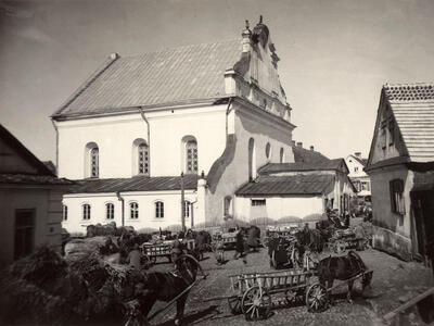 Exterior photograph of buildings on busy street with horses pulling wagons.