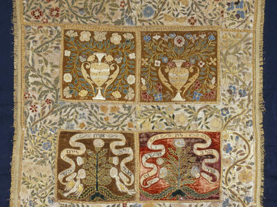 Cloth embroidered with floral border, and four central panels, the top two with pitchers, vines, and flowers, and the bottom two with trees and ribbons with Hebrew text. 