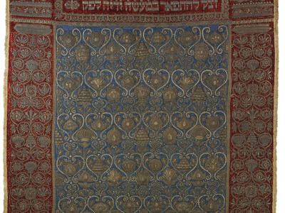Cloth embroidered with floral border, Hebrew text across the top, and repeating motif in center. 
