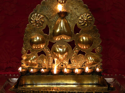 Oil lamp with row of eight cups on the bottom and scallop-shaped decorations.