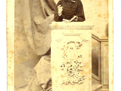 Photograph of young man wearing a hat and standing behind a podium.