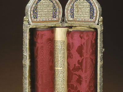 Ornately decorated cylindrical case with Hebrew writing on top and scroll inside; closed cylindrical case with ornate decoration.