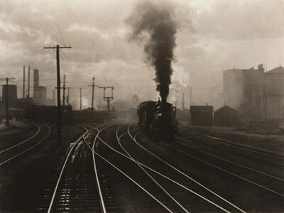 Photograph of train on tracks with large smoky cloud above it.