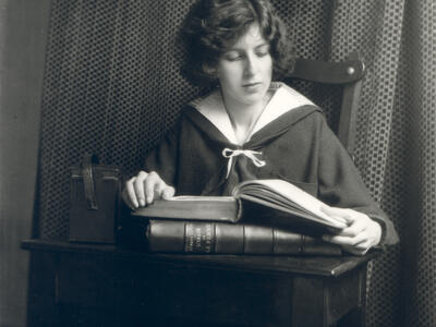 Photograph of figure seated at desk reading a book.