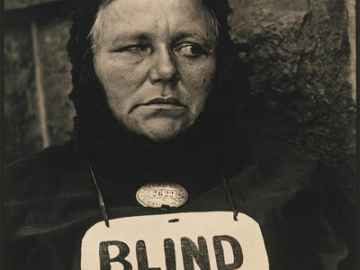 Photograph of woman wearing a sign around her neck that reads "BLIND."