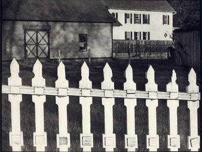 Photograph of fence in foreground and two houses in background.
