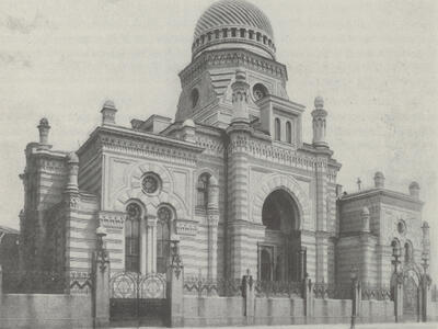 Street view of ornate building with archways, turrets, and domed roof, surrounded by fence.