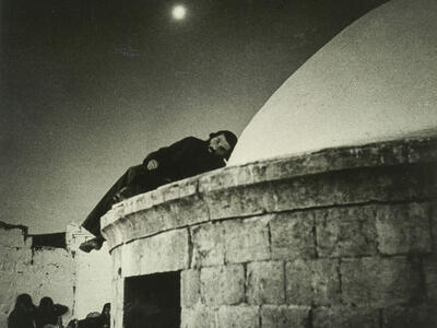 Photograph of man lying on domed roof of stone building.