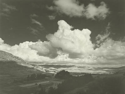 Photograph of valley with buildings under cloudy sky.