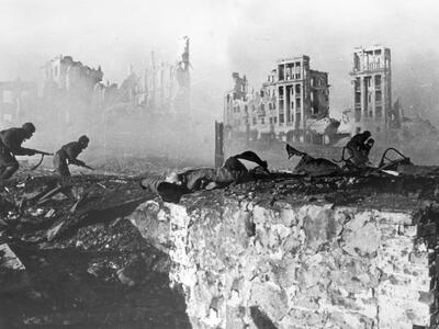 Photograph of soldiers holding guns as they approach ruins of a bombed city. 