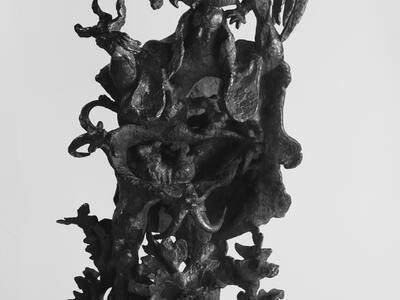 Bronze sculpture depicting a standing man, surrounded by harsh foliage and holding a rooster above his head. 