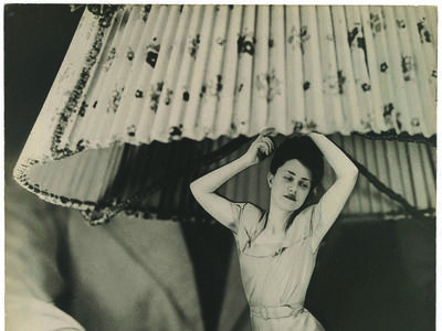 Photomontage featuring male hand grabbing the base of a lamp. The lamp base is a woman wearing a dress.