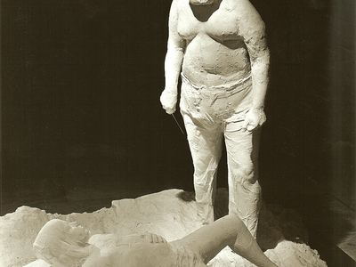Sculpture of a man standing over a boy lying on his back. 