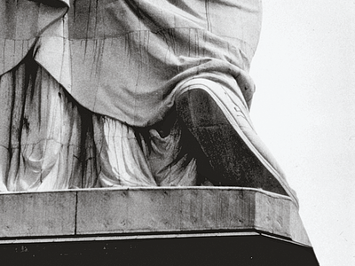 Photograph depicting pedestal of large sculpture with people standing around its base.