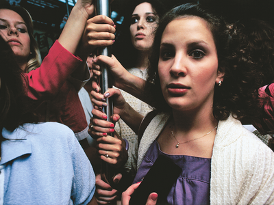 Photograph featuring women standing holding on to a subway pole. 