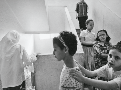 Photograph featuring four young girls holding onto each other's shoulders walking down the stairs in a train with two older women in the front and back.