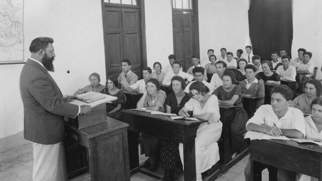 Tanakh Class in Jaffa Photograph of classroom with teacher at podium and men and women at rows of desks.