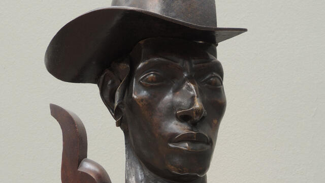 Bust of man wearing a hat.