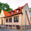 Front view of building exterior with curved tile roof and arched windows and metal fence around perimeter. 