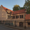 Rear view of exterior building with curved tile roof, arched windows and metal fence around perimeter. 