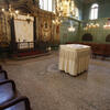 Photograph of room with benches along perimeter of wall and decorated walls, with small central table covered with cloth. 